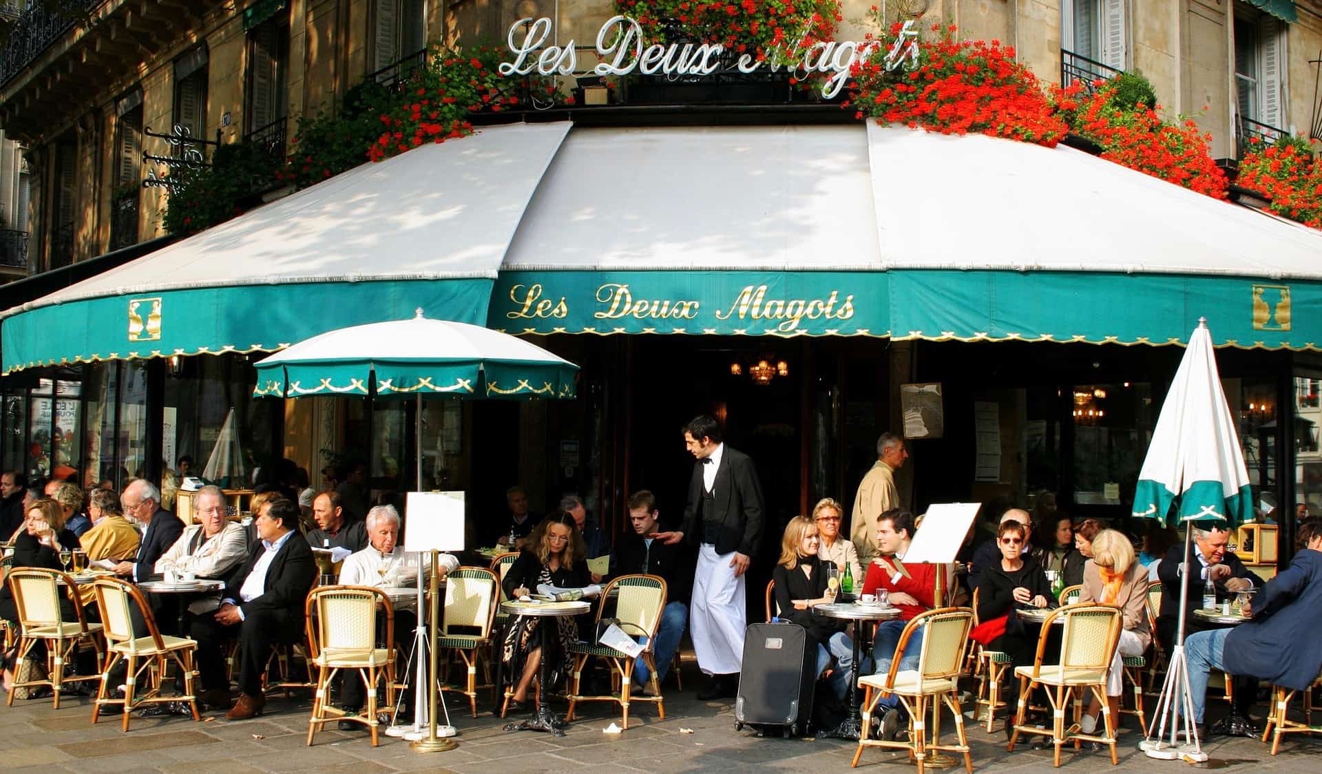 Moradores e turistas relaxam em Les Deux Magots em Paris, França