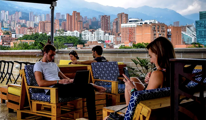 Pessoas sentadas em um terraço ao ar livre com o horizonte de Medellín ao fundo no Los Patios Hostel em Medellín.