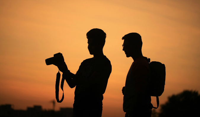 Dois fotógrafos ao pôr do sol olhando para a câmera enquanto fotografam