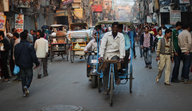 Uma rua movimentada de uma cidade indiana cheia de gente e riquixás.