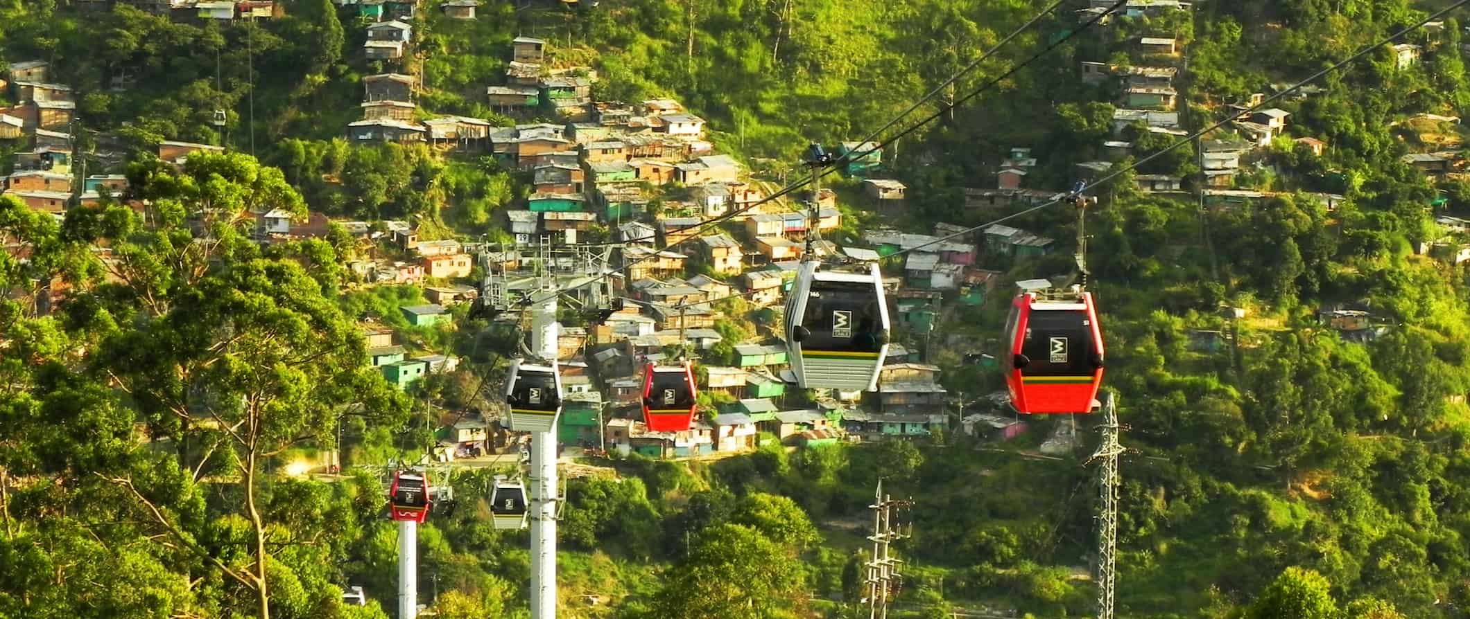 Vista dos teleféricos em Medellín, Colômbia, cercados por uma vegetação exuberante e pequenas casas construídas na encosta da montanha