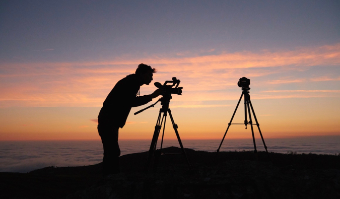 Um homem tira fotos na montanha com duas câmeras grandes ao nascer do sol