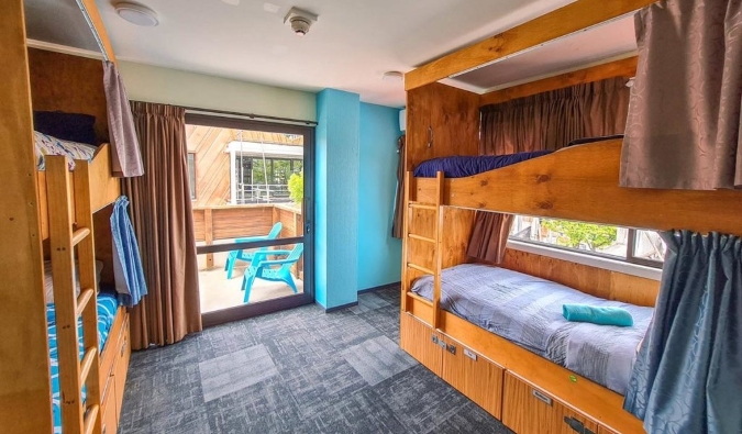 Beliches de madeira com cortinas para privacidade em um quarto bem iluminado no Adventure Queenstown Hostel em Queenstown, Nova Zelândia