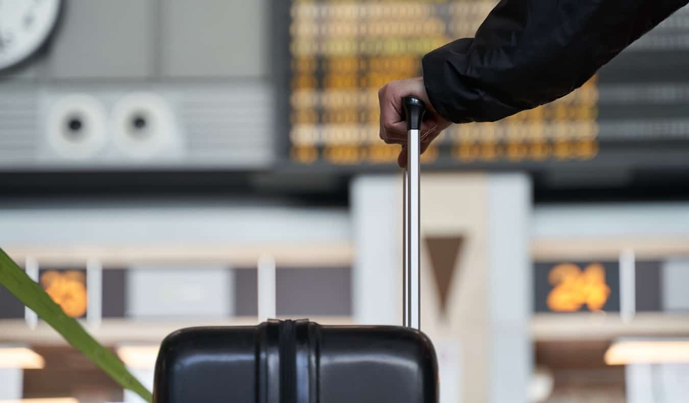 Uma pessoa segura a alça de uma mala rolante, olhando para as missões no aeroporto