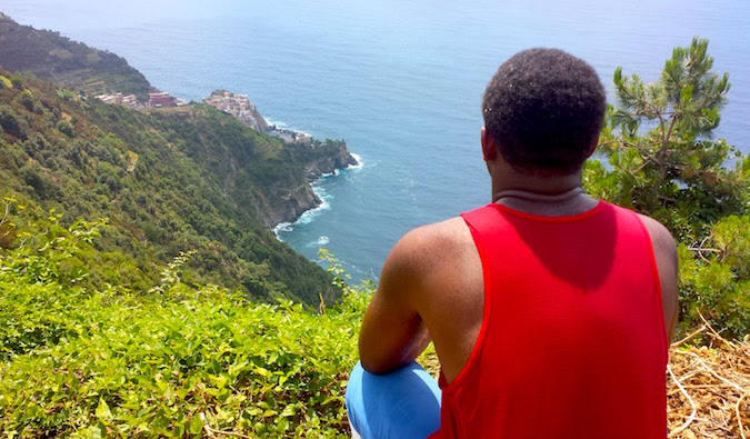 Viajante masculino solitário senta-se em uma rocha e admira a vista para o mar