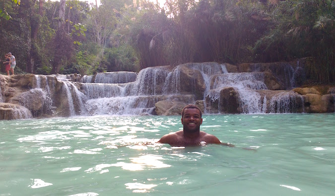 Viajante negro sozinho nada em piscina com cachoeira na Ásia