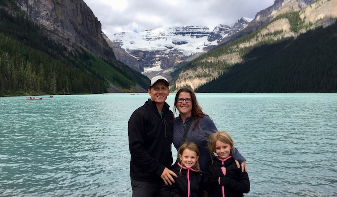 Amanda e sua família de viajantes posando perto do lago com montanhas ao fundo