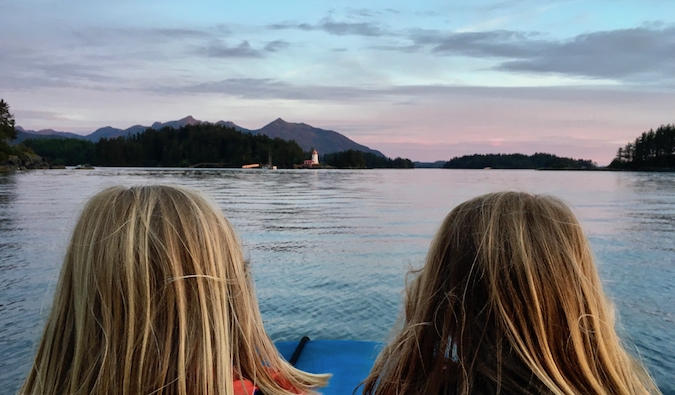 Dois jovens viajantes posam na água ao pôr do sol