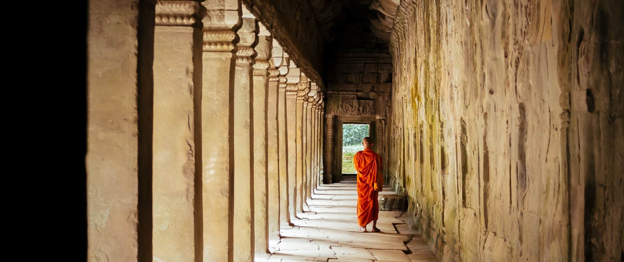 Um monge com uma túnica laranja caminha por um templo