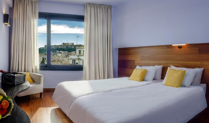 Um quarto de hóspedes no Atenas Center Square Hotel com uma janela aberta da qual a Acrópole à distância é visível