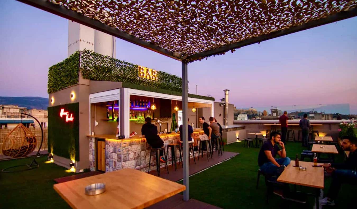 Pessoas relaxam no bar da cobertura do Hawks of Athens Hostel, na Grécia, durante o pôr do sol.