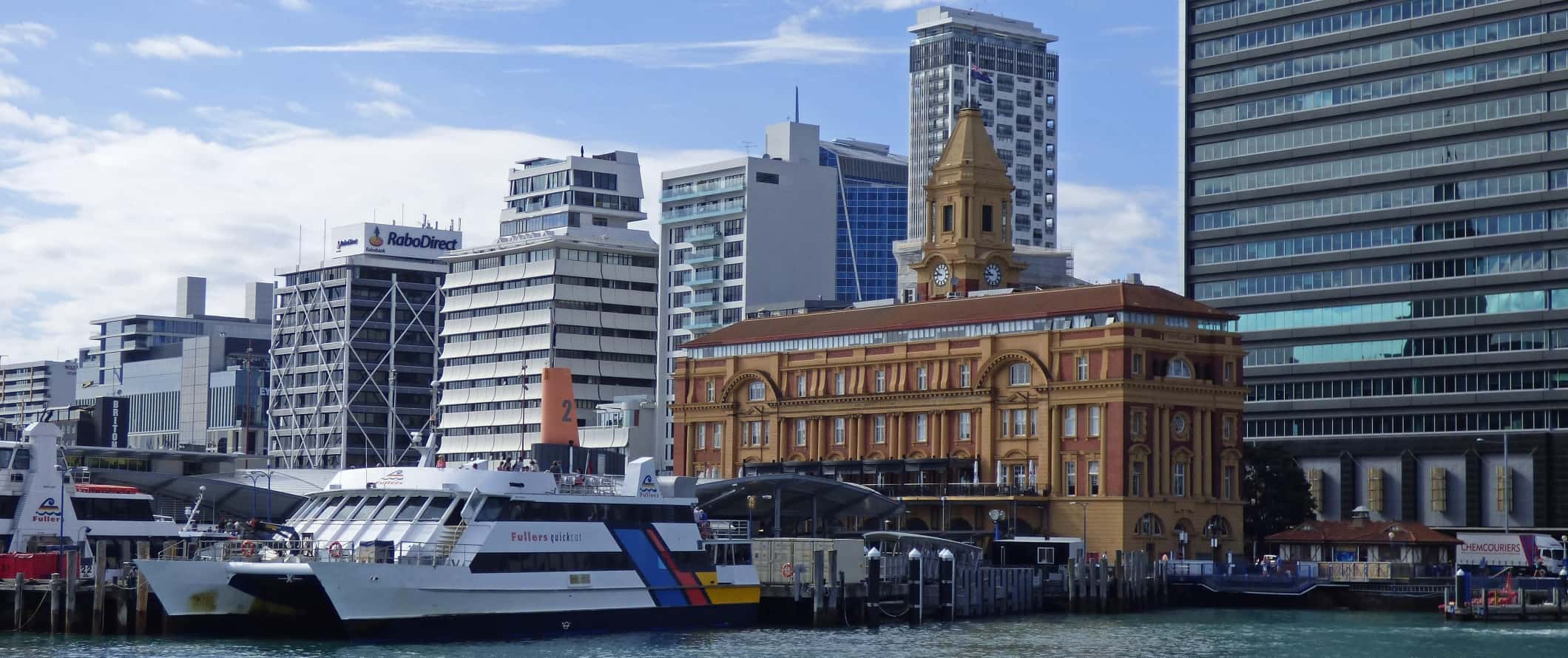Orla marítima do porto com balsa, edifício histórico e arranha-céus altos ao fundo em Auckland, Nova Zelândia.