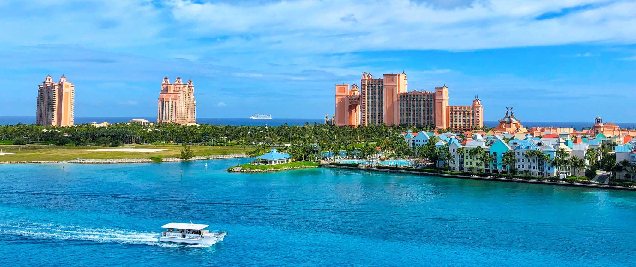 O complexo hoteleiro Atlantis ao fundo com um barco navegando pelas águas azuis brilhantes em primeiro plano, nas Bahamas
