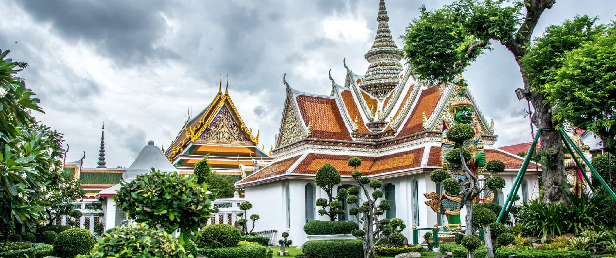 Edifícios dourados do complexo do templo de Wat Arun, cercado por topiaria be m-enlutada em Bangcoc, Tailândia