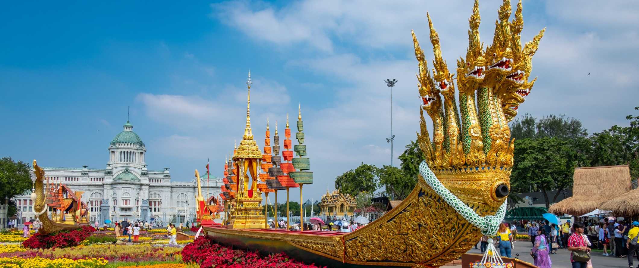 Uma grande barcaça de ouro longa com muitas cabeças de dragões fica em um canteiro de flores brilhantes em frente ao Museu Royal Barge em Bangkok, Tailândia