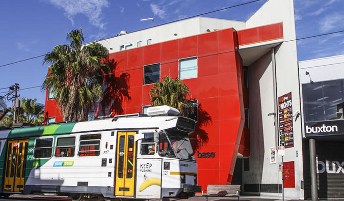 Exterior vermelho da base de base do albergueKilda com um bonde passando na frente dele, em Melbourne, Austrália