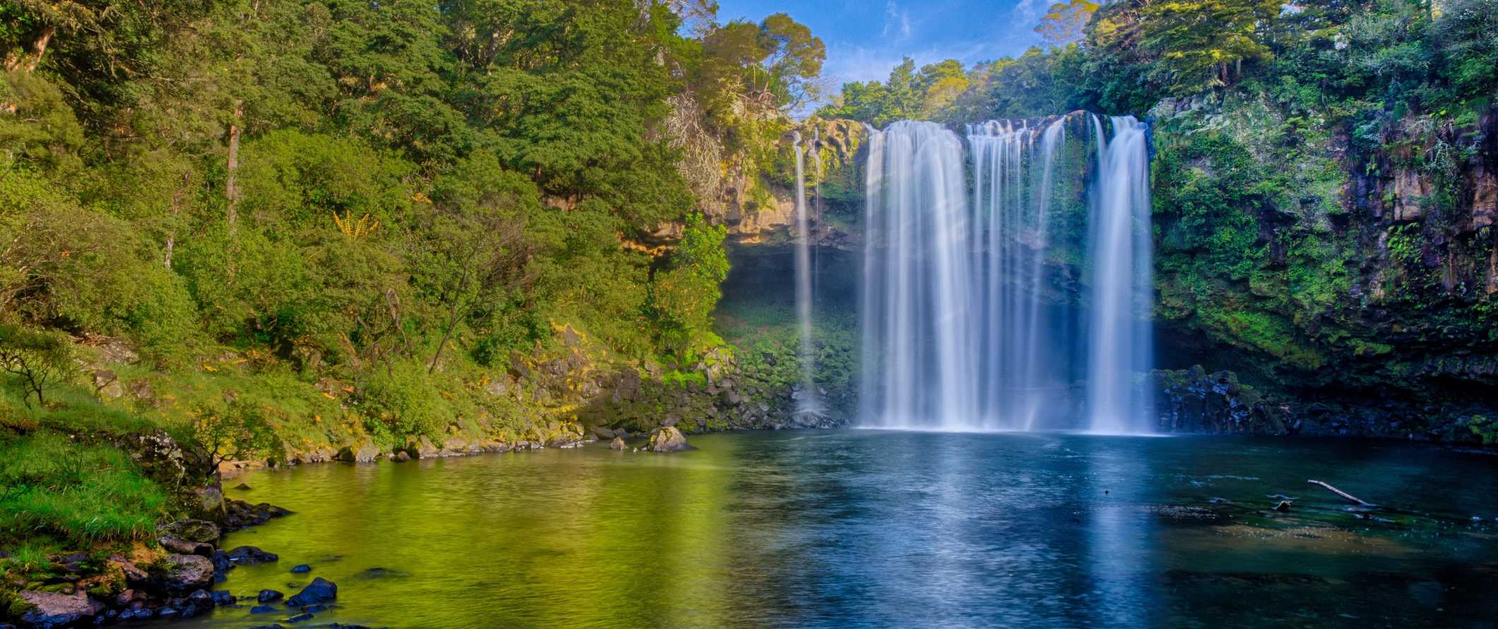 Rainbow da cachoeira - uma cachoeira pitoresca que leva a uma grande piscina na floresta na baía das ilhas, Nova Zelândia