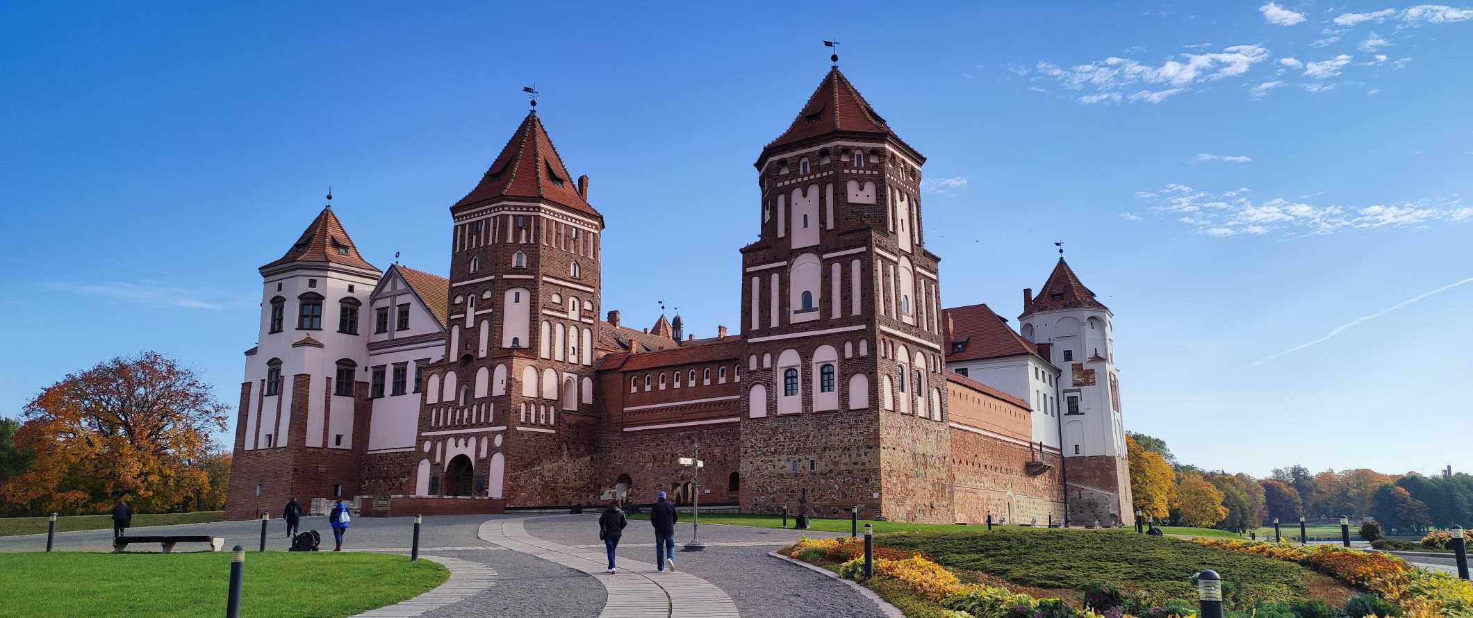 As pessoas andam por um caminho inclinado que leva a um castelo mundano, um impressionante castelo de tijolos vermelhos na Bielorrússia