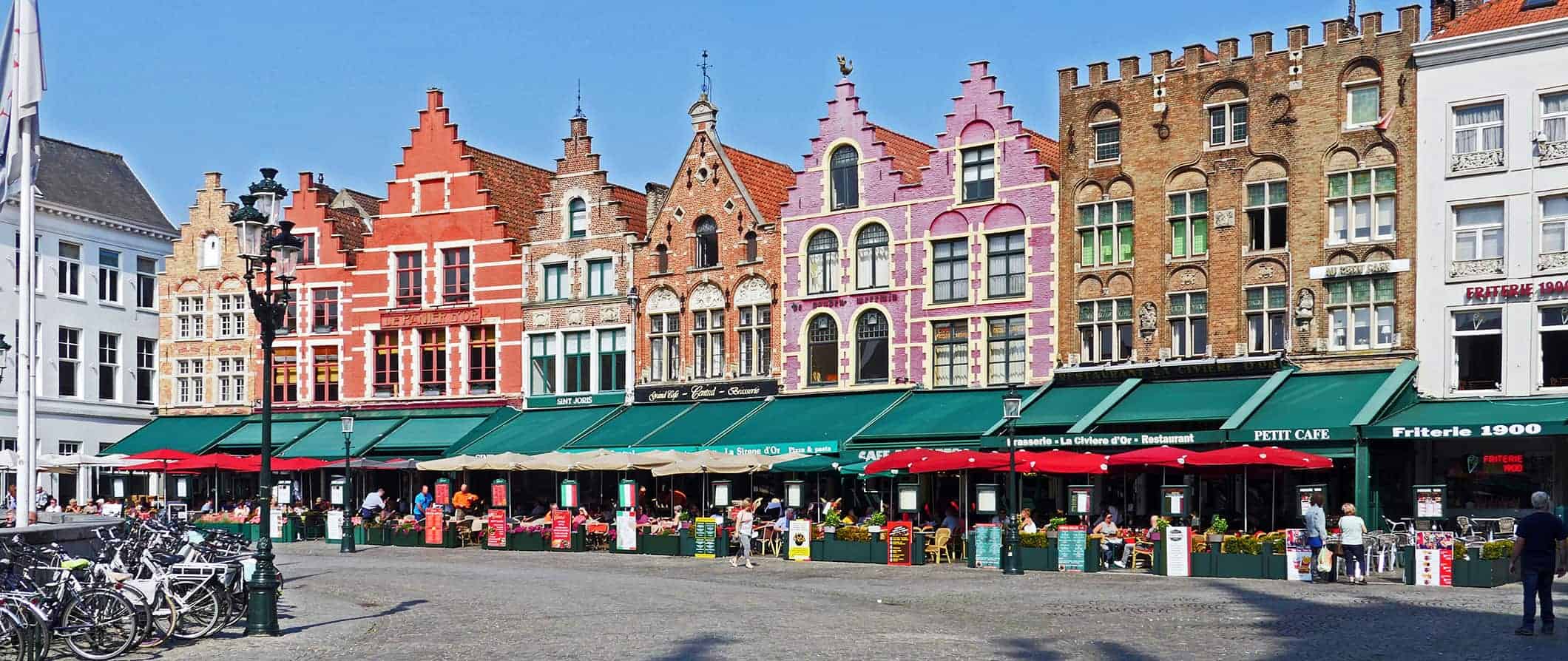 Uma rua multifolorada com casas antigas em Bruges, Bélgica, ao lado de uma área cheia de pessoas