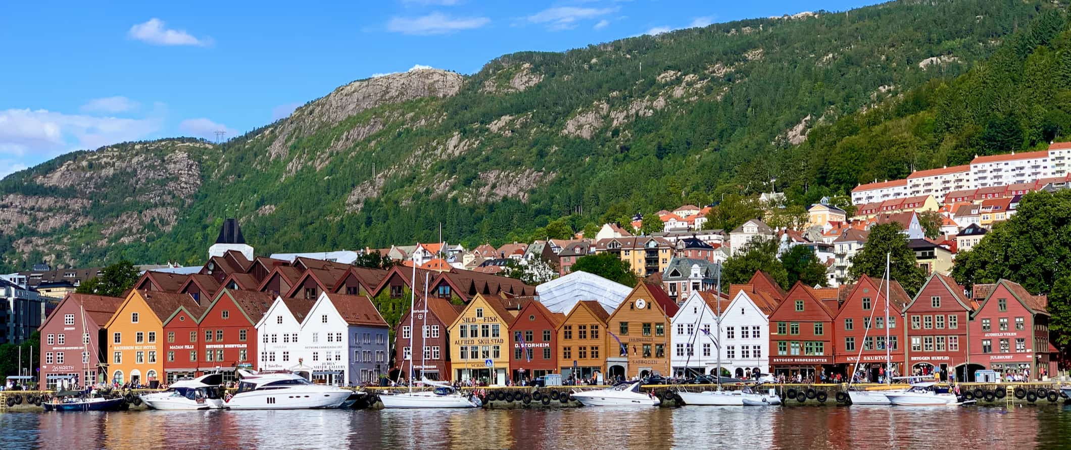 Vários edifícios antigos de colorção mult i-colorida ao longo das margens calmas de Bergen, Noruega