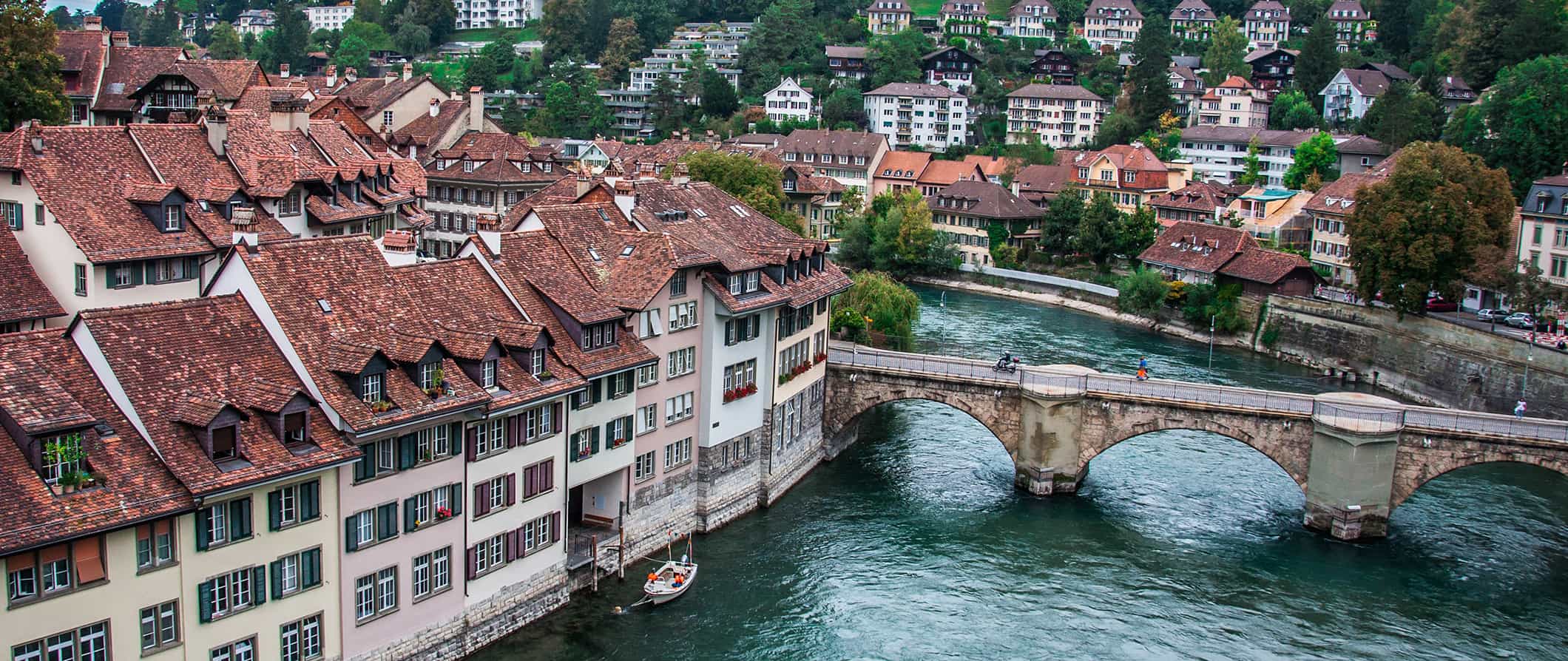 Edifícios encantadores de Berna, Suíça, ao longo do rio com casas numa colina ao fundo