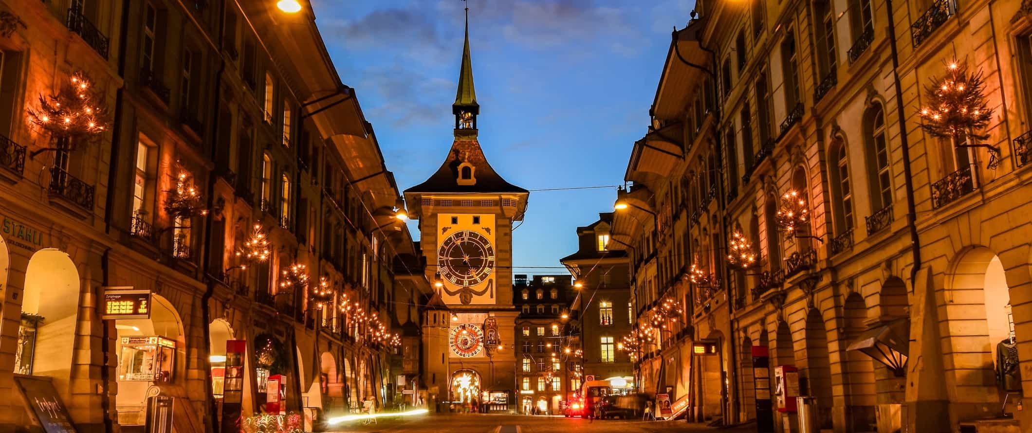 Rua espaçosa com uma histórica torre do relógio no final iluminada à noite em Berna, Suíça