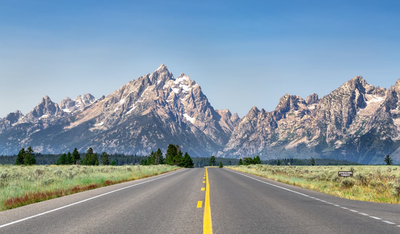 Open Road em um dia ensolarado em Wyoming, EUA, com montanhas ao fundo