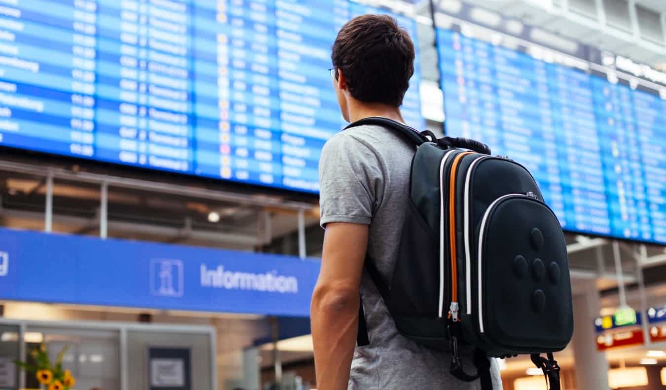 Um jovem com uma mochila no aeroporto analisa o cronograma de voo