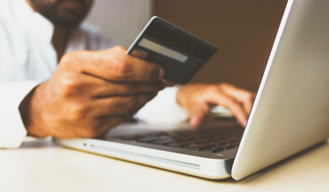 Um homem em um laptop usa um cartão de crédito para compras na internet