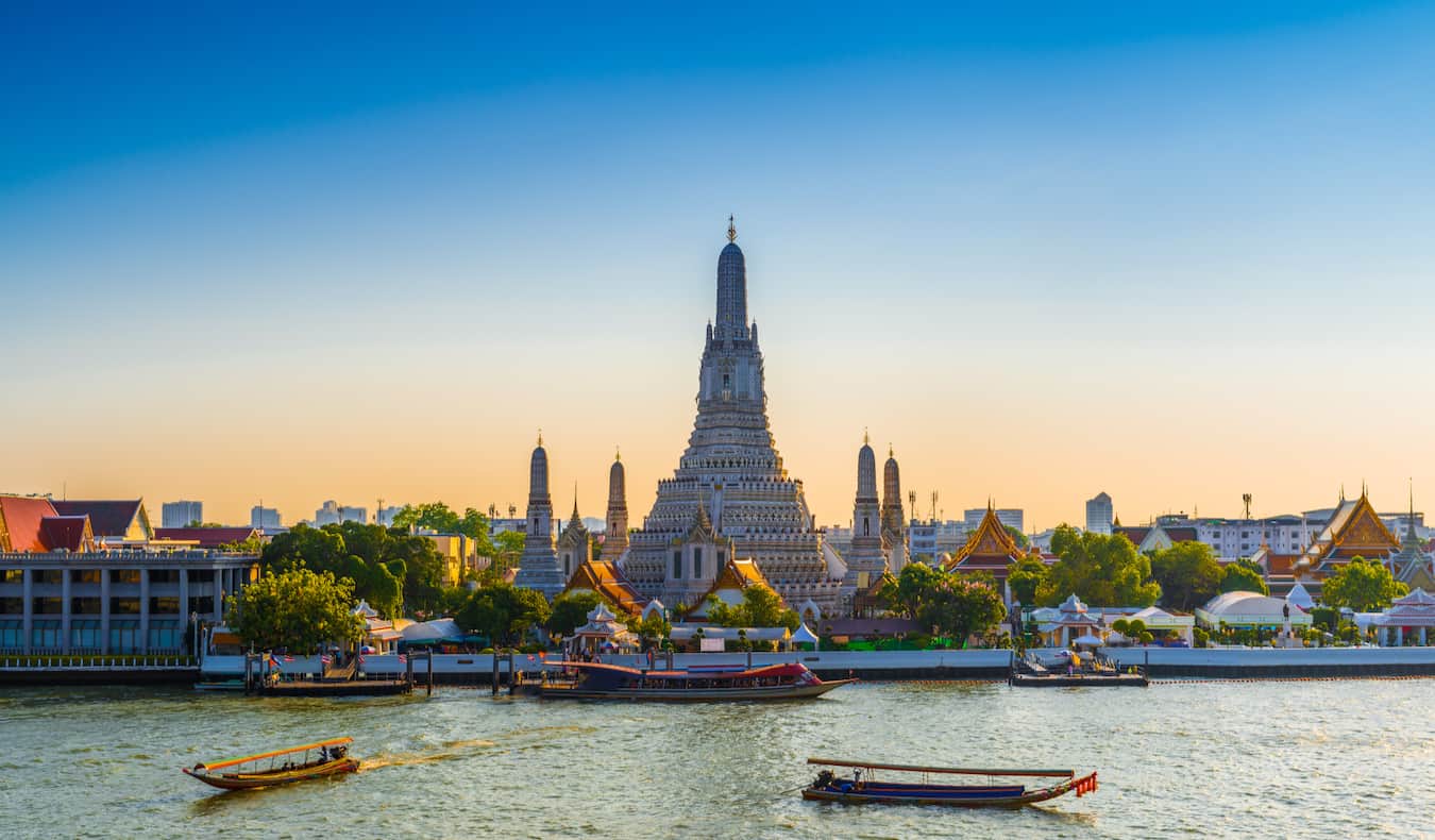 Cruzeiro no rio em Bangkok, Tailândia, com um templo histórico do outro lado do rio no fundo