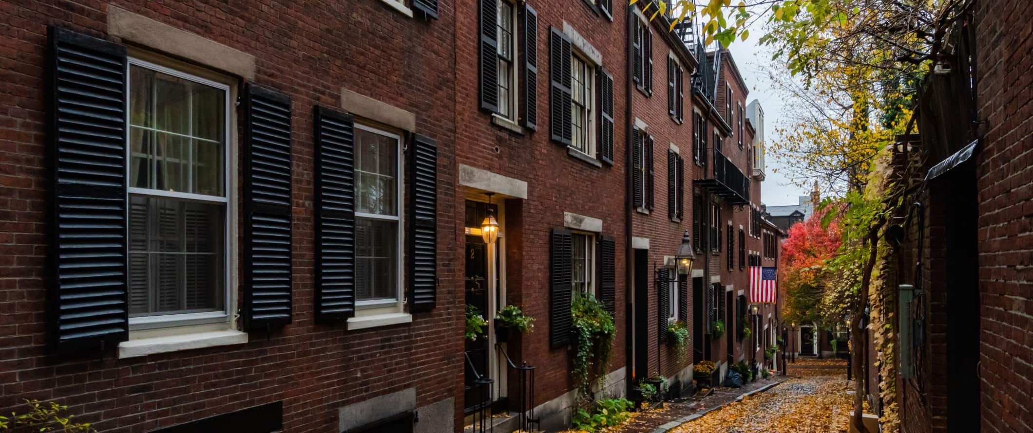 Historical Brick abriga persianas pretas no beco com folhas de laranja no chão em Boston, Massachusetts.