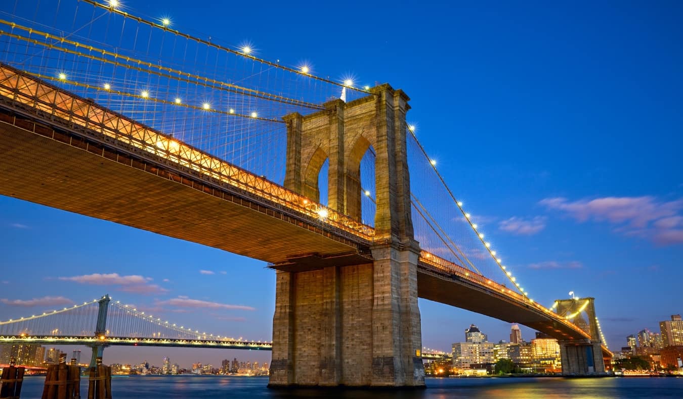 O vôo completo da ponte do Brooklyn contra o fundo do horizonte de Manhattan, iluminado à noite em Nova York, EUA.