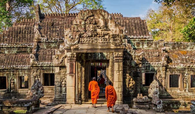 Dois monges em roupas laranja caminham pelo templo no Camboja