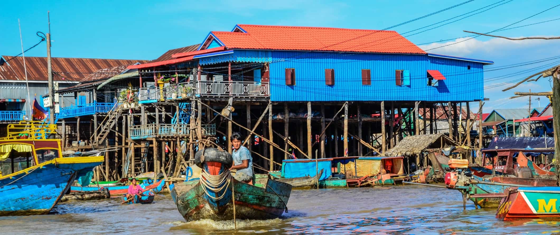 Um homem navega em um barco ao longo de um canal em frente a palafitas pintadas em cores vivas em Tonle Sap, Camboja.