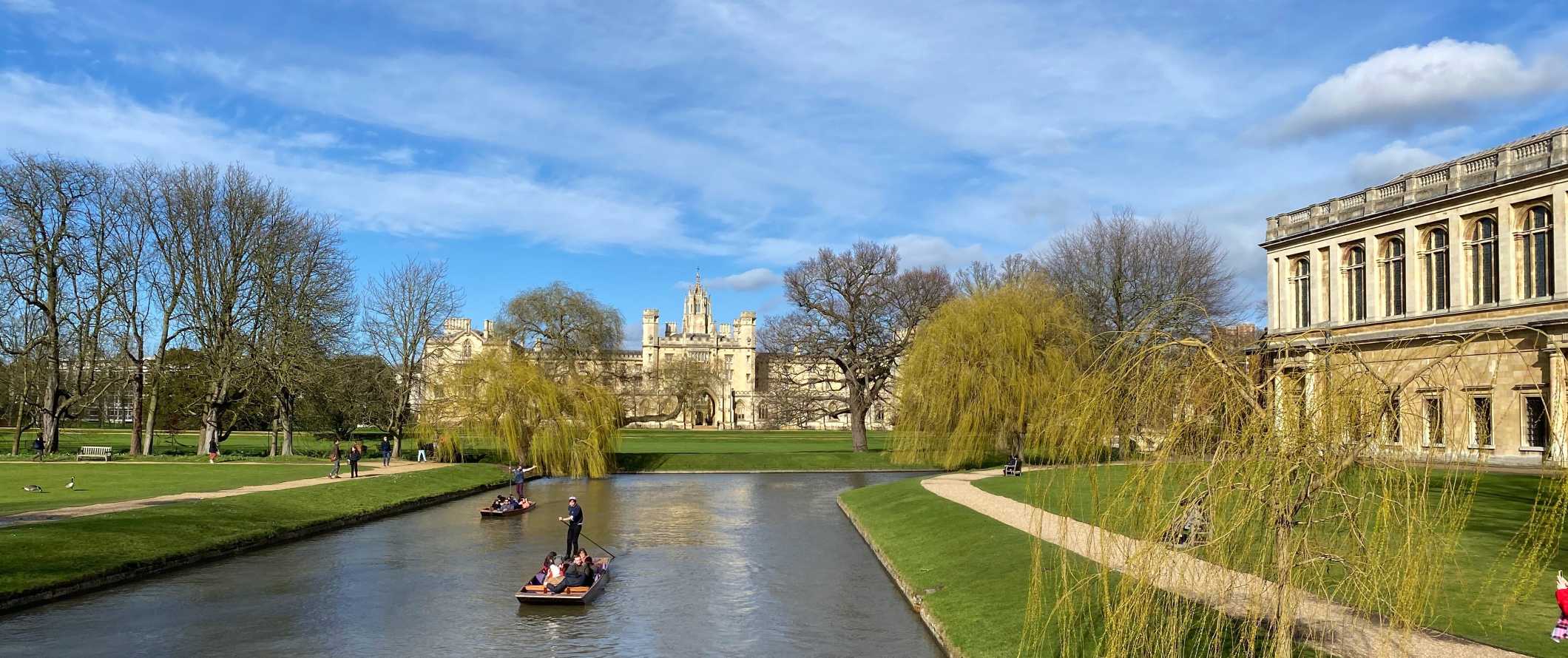 As pessoas andam de barco no rio com edifícios da Universidade de Cambridge em segundo plano em Cambridge, Inglaterra