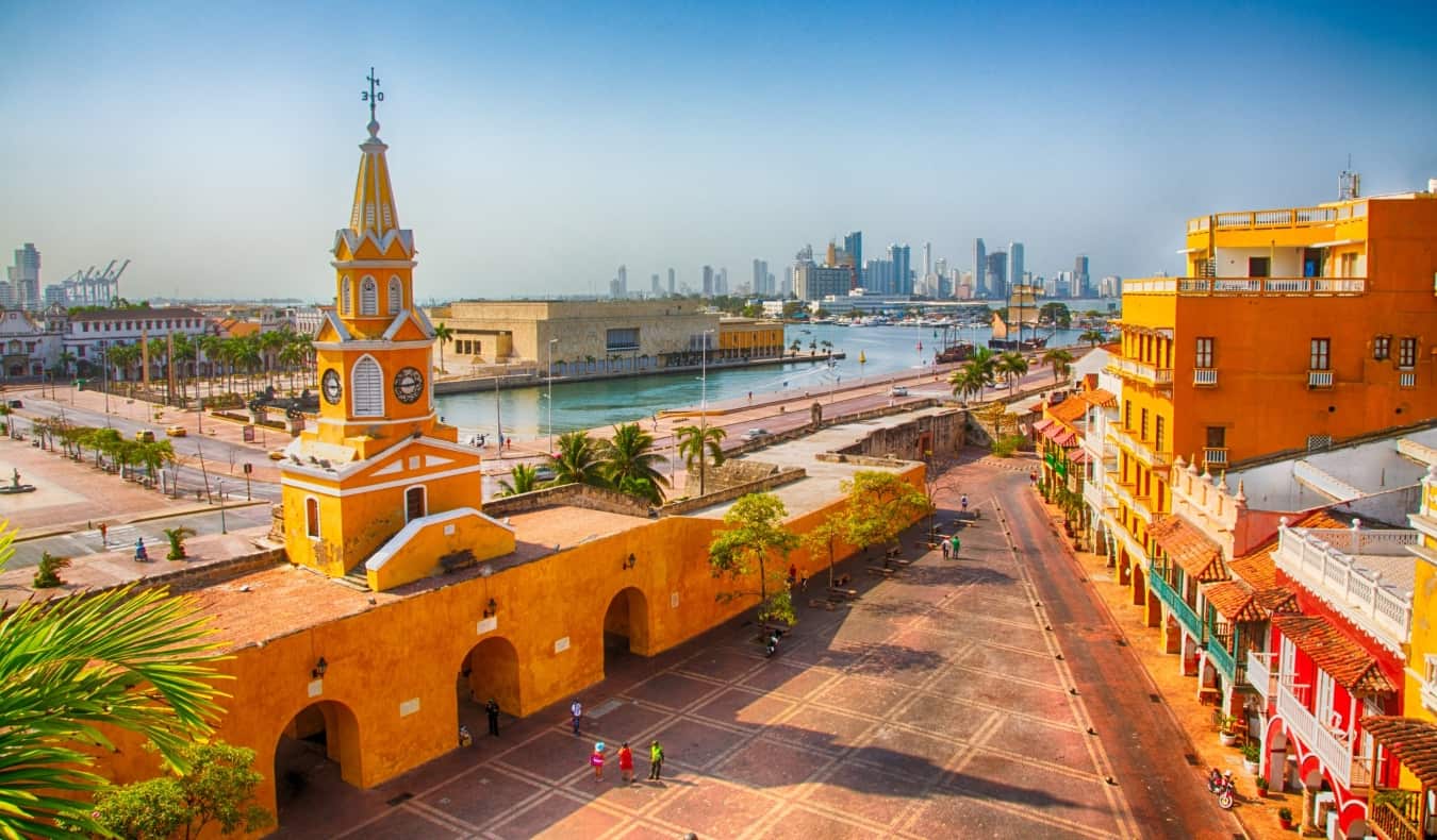 Vista da vasta área cercada por edifícios históricos de laranja brilhante, com um porto e arranh a-céus modernos em segundo plano em Cartagena, Colômbia
