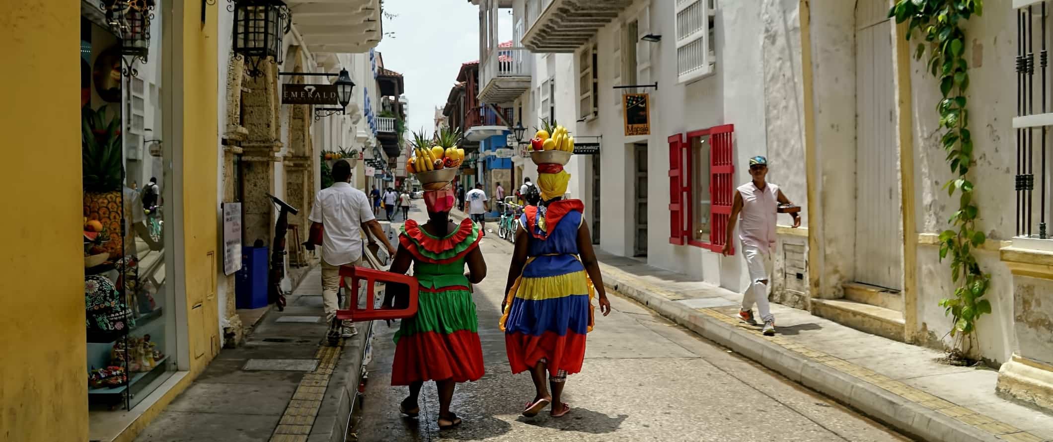 Duas mulheres em vestidos brilhantes e coloridos caminham pela rua com cestas de frutas na cabeça em Cartagena, Colômbia