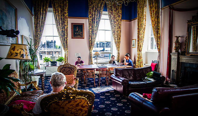Sala comum aconchegante com sofás de couro, poltronas grandes, mesa comunitária e janelas altas no Castle Rock Hostel em Edimburgo