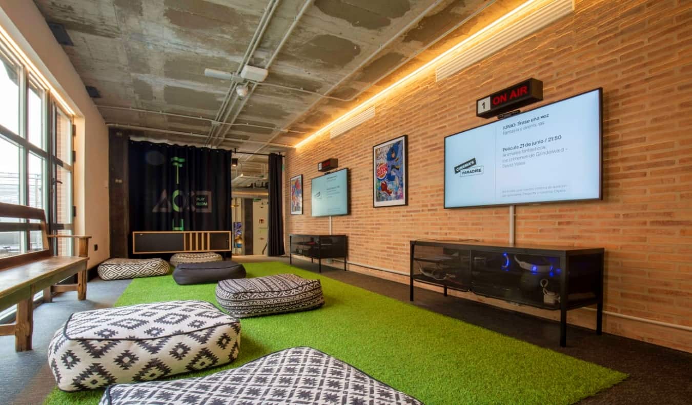 Uma sala de jogos com grandes televisões de ecrã plano e muitos pufes no hostel The Central House Lavapies, em Madrid, Espanha.