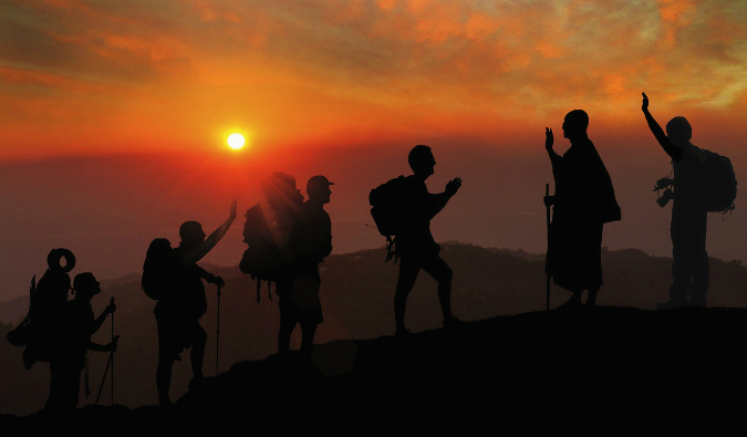Um grupo de viajantes sobe uma montanha durante um pôr do sol brilhante