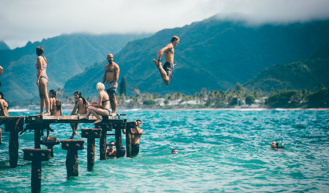Um grupo de viajantes mergulha de um cais em um dia ensolarado.