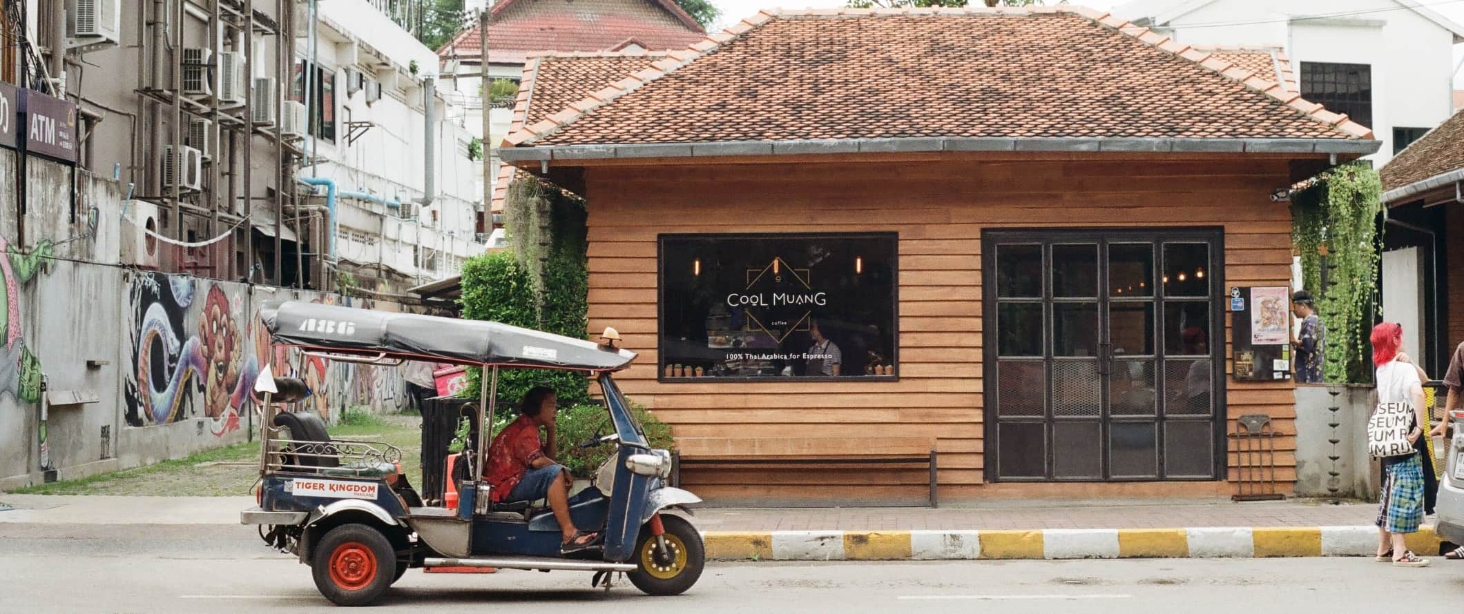 Uma pessoa dirige em Rickshaw passa por uma cafeteria quando as pessoas caminham pela rua em Chiangmai, Tailândia