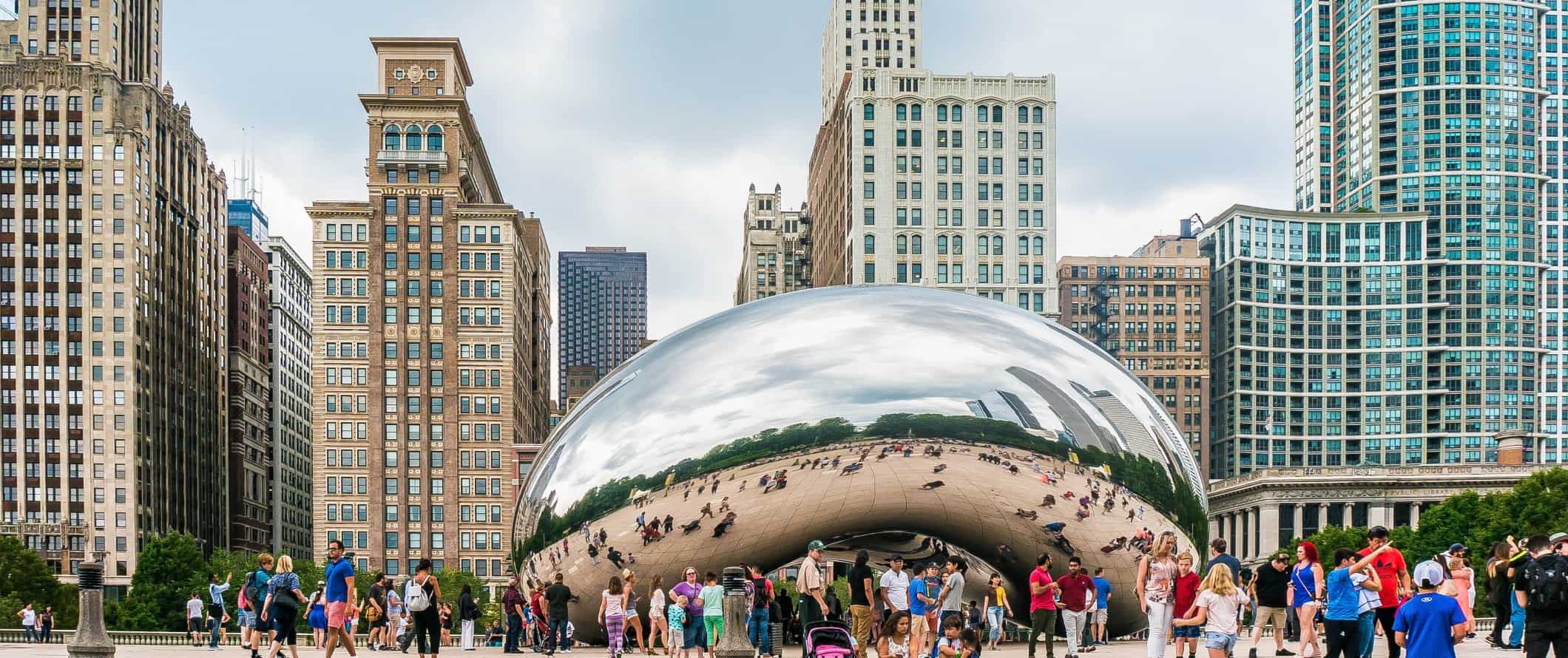 Um enorme bob cromado reflexivo com pessoas ao redor e edifícios altos atrás dele em Chicago, EUA.