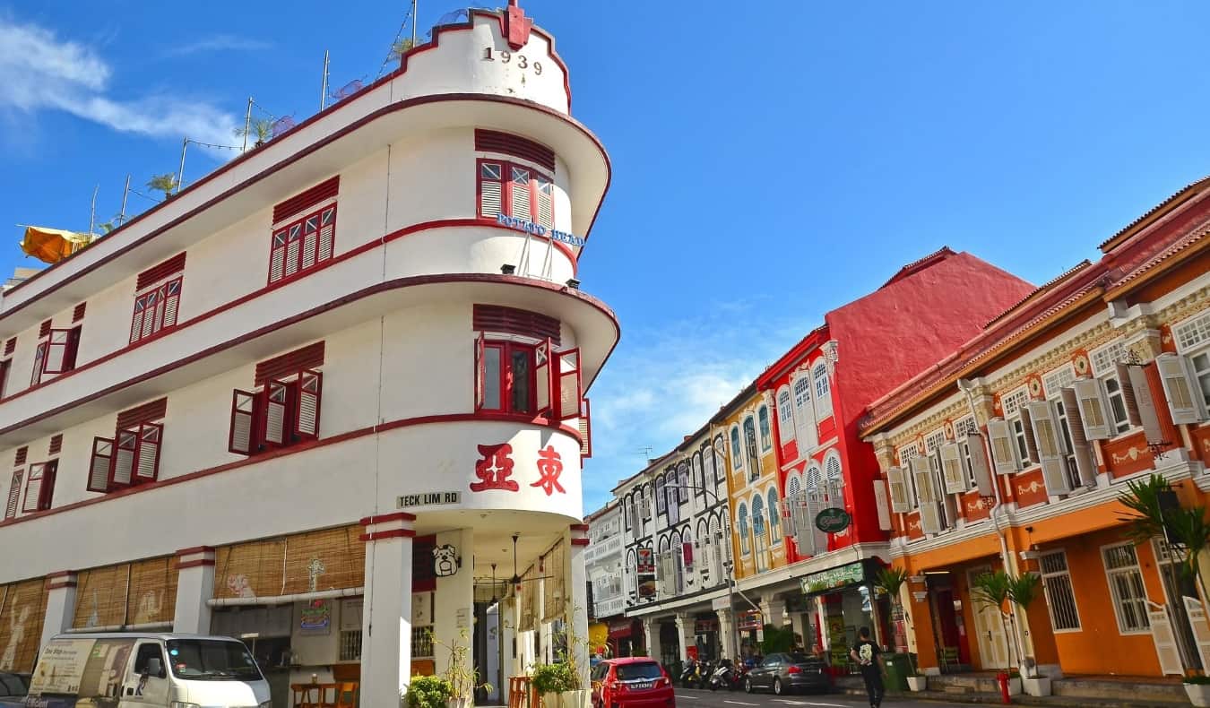 Um edifício branco de formato triangular, enfeitado com tinta vermelha e decorado com caracteres chineses, em uma rua com outros edifícios coloridos em Chinatown, Cingapura
