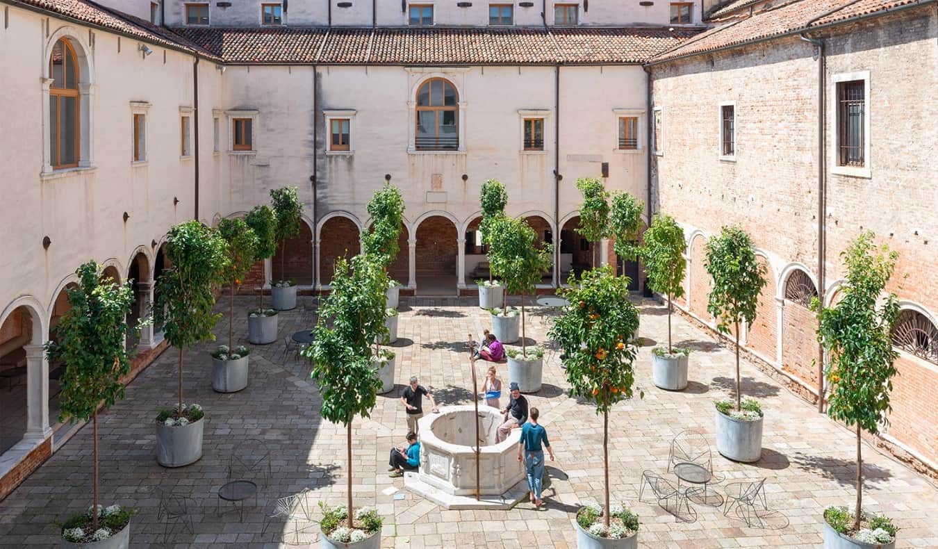 Um mosteiro histórico com laranjeiras e pessoas que ficam e conversam no albergue da Combo Venezia em Veneza, Itália.