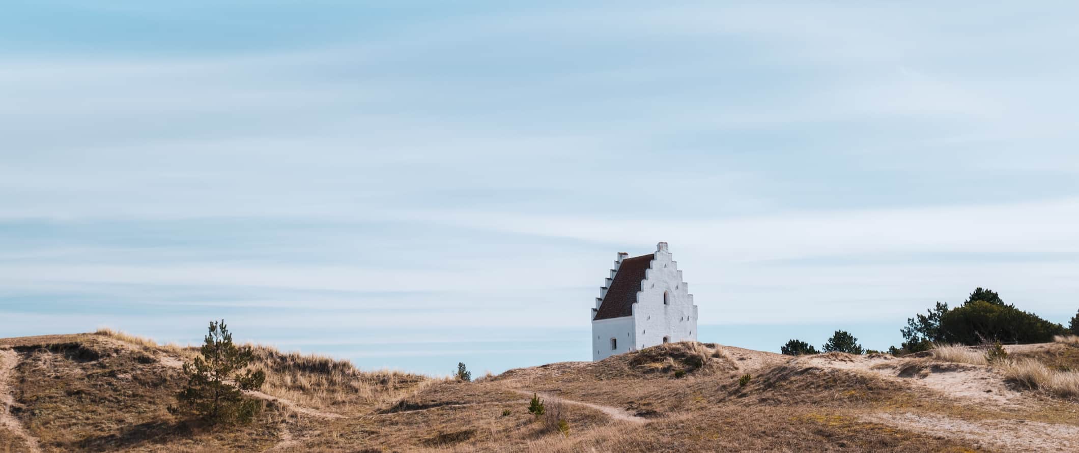 Uma pequena igreja branca na costa acidentada e varrida pelo vento da Jutlândia, na Dinamarca