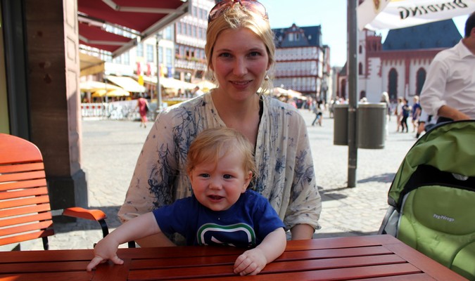 Mãe com um bebê sent a-se em uma mesa de piquenique vermelha na rua na Europa