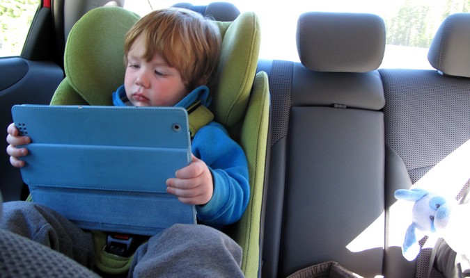 O garoto brinca com a eletrônica no banco de trás durante uma viagem em família