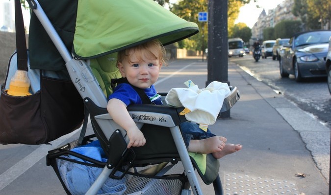 Bebê doce sorri em uma câmera em um carrinho enquanto viaja para o exterior
