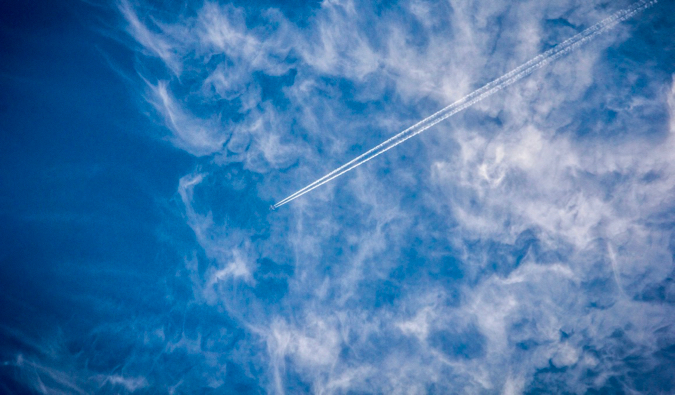 Avião comercial no alto do céu, cortando as nuvens e o céu azul